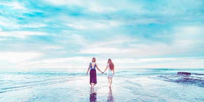 两个女人走在海岸线牵手
